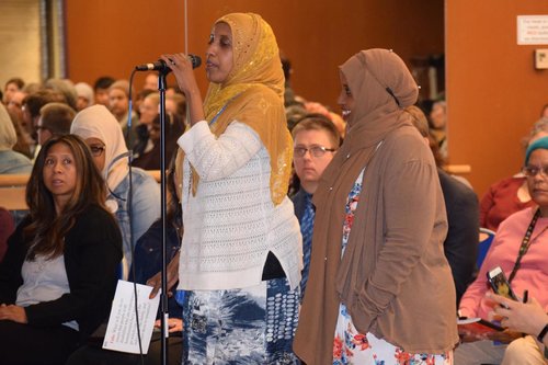 Two women in hijabs asking questions at a candidate forum.