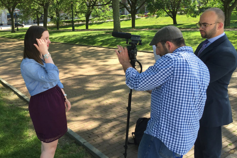 Two men filming a young woman speaking