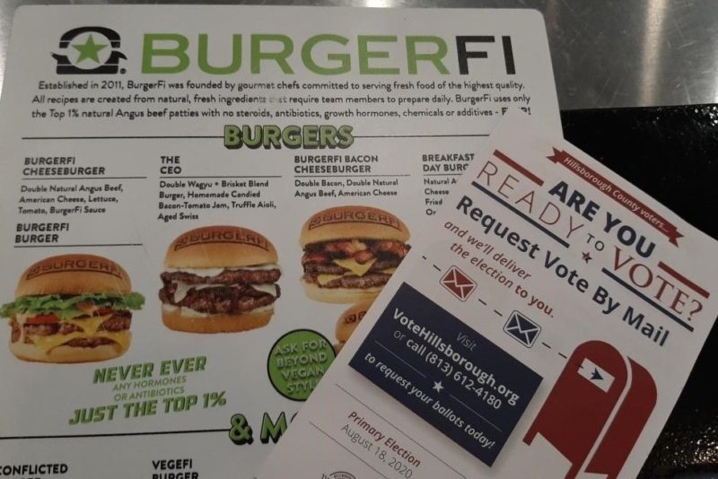 A burger restaurant menu next to a vote-by-mail flyer