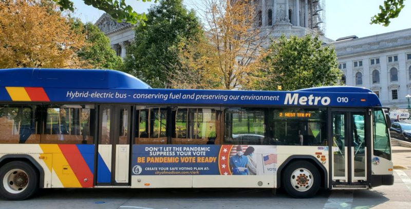 A public bus has an advertisement posted on it that reads, "Be Pandemic Vote Ready"