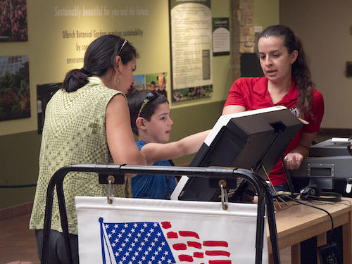 An election officer stands next to a child and a parent at a voting machine