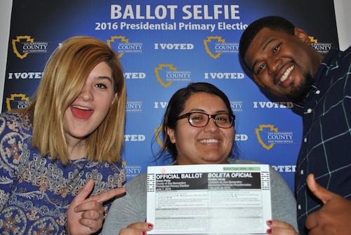 Three young people hold up an unofficial ballot and smile for a photo.