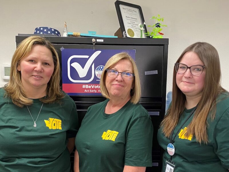 Three women with green shirts that say "Vote" pose for a photo