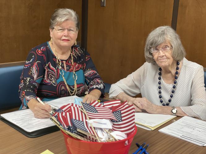 two women pose at a desk with paperwork and American flags.