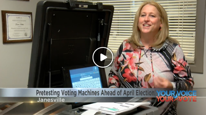 In a screenshot from a news clip, a woman stands in front of a voting machine