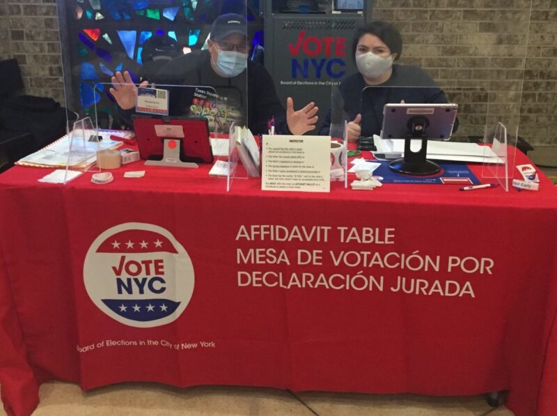 two people with masks sitting at a table that says "Affidavit Table" pose for a photo