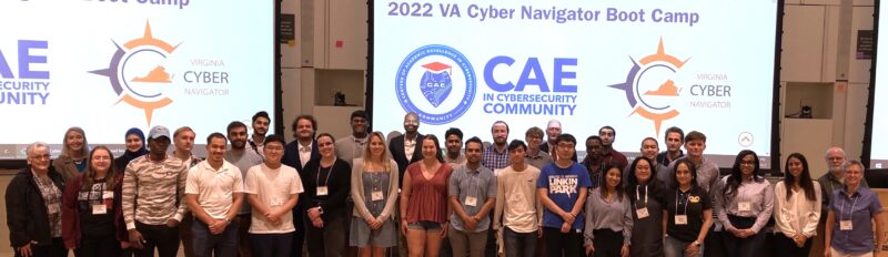 A group of about 35 people pose in front of a screen that says "2022 VA Cyber Navigator Boot Camp"