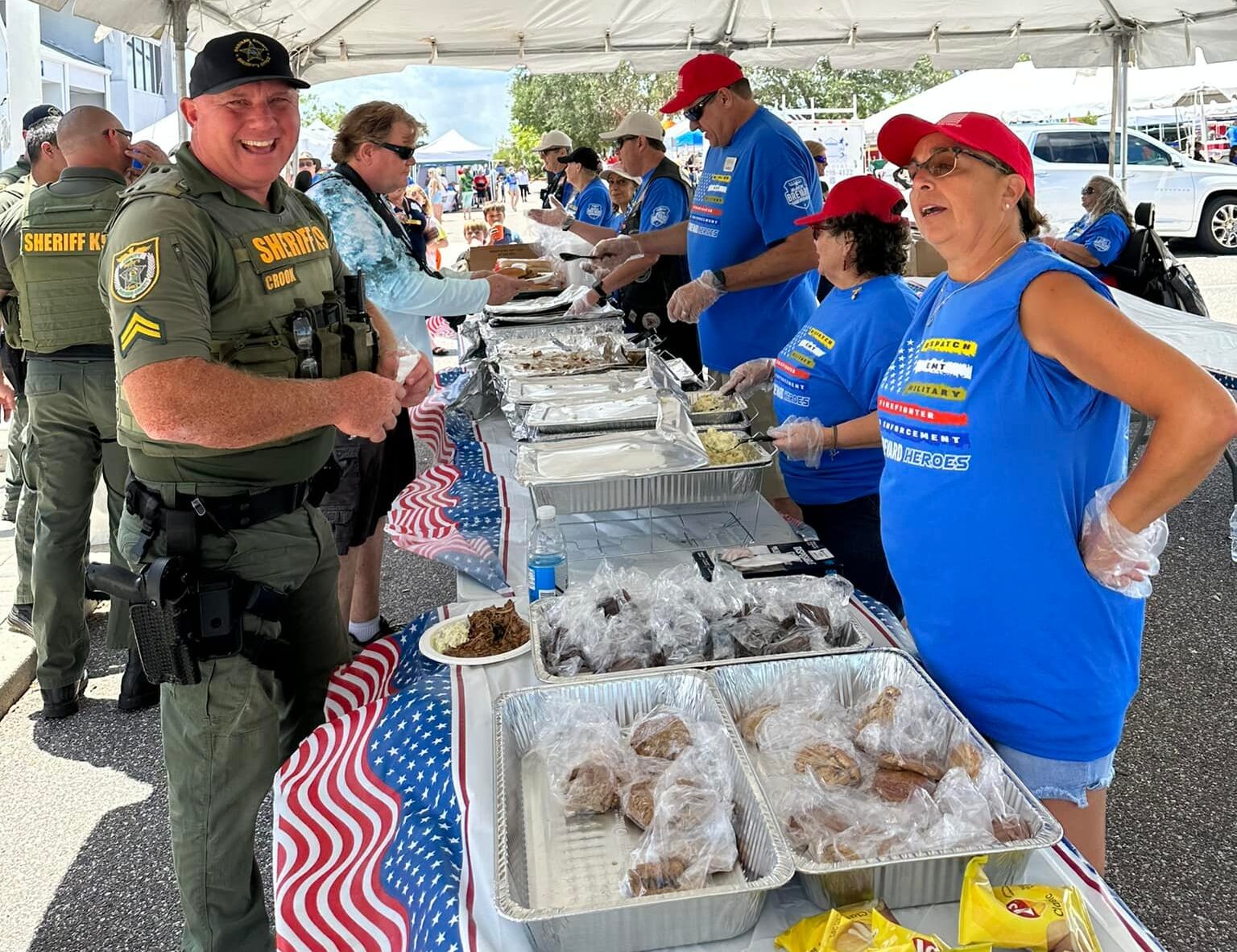 People dressed in matching blue t-shirts and red hats serve food to a smiling man in a uniform.